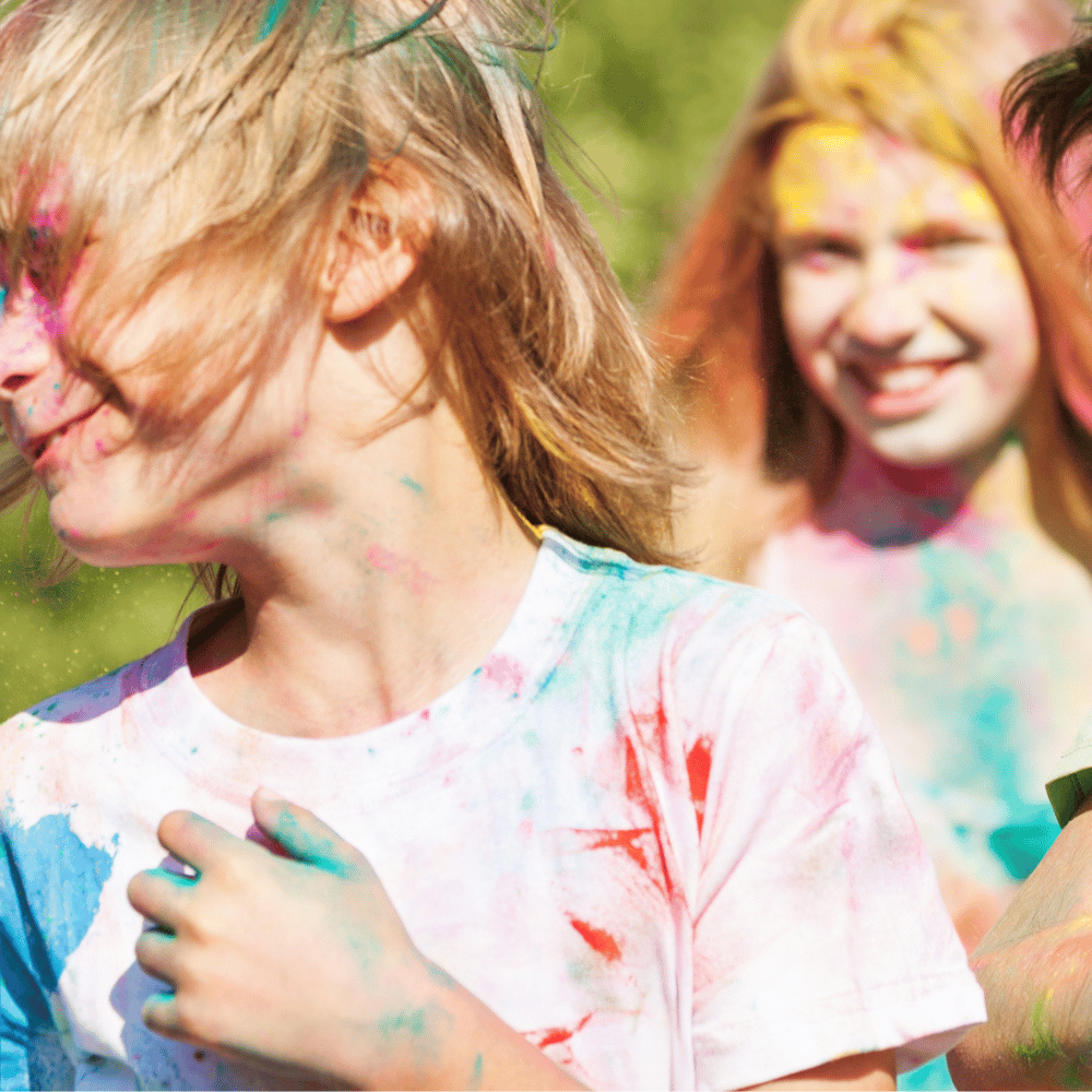 A boy wearing a white t-shirt with colour powders on it